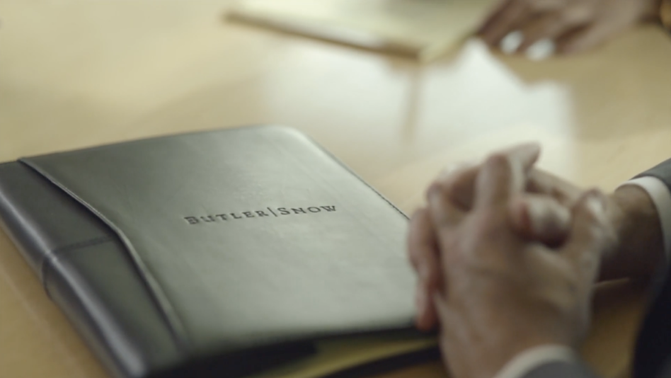 A table with a leather folder with Butler Snow embossed on it, and hands clasped together beside it.