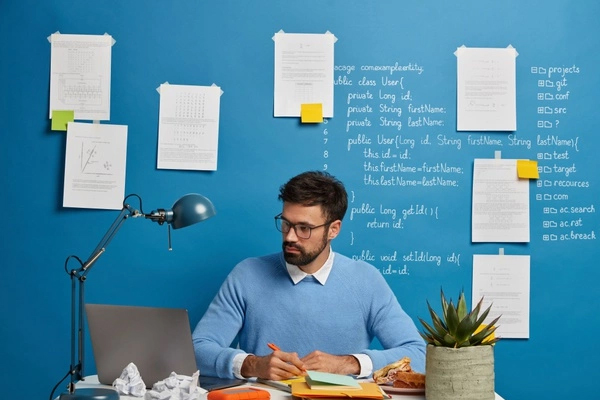 man sitting at desk with papers and writing on the wall behind him