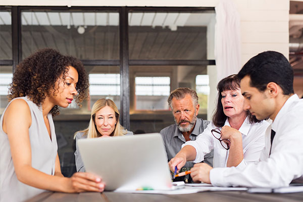 group of five people sitting at a table looking at a computer