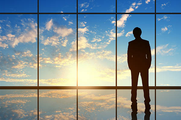 person standing inside by a window, staring at sunset